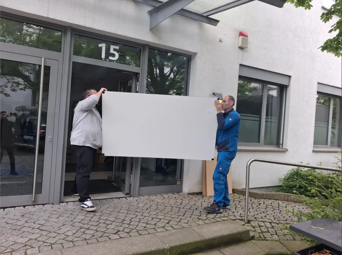 Mitarbeiter tragen gemeinsam eine große Tischplatte aus einem Gebäude